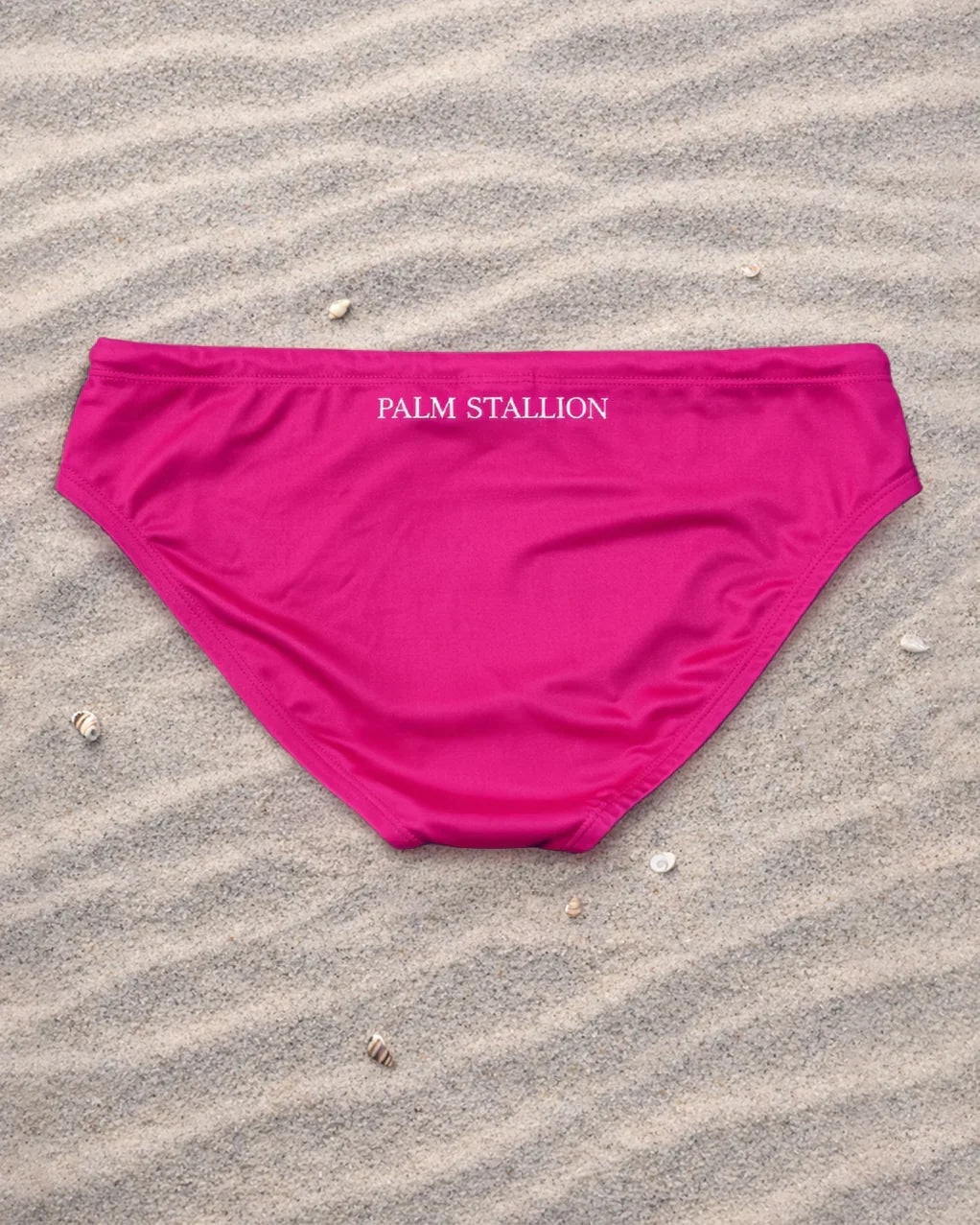 Palm Stallion pink swim briefs back view on sand with seashells, beachwear swimwear