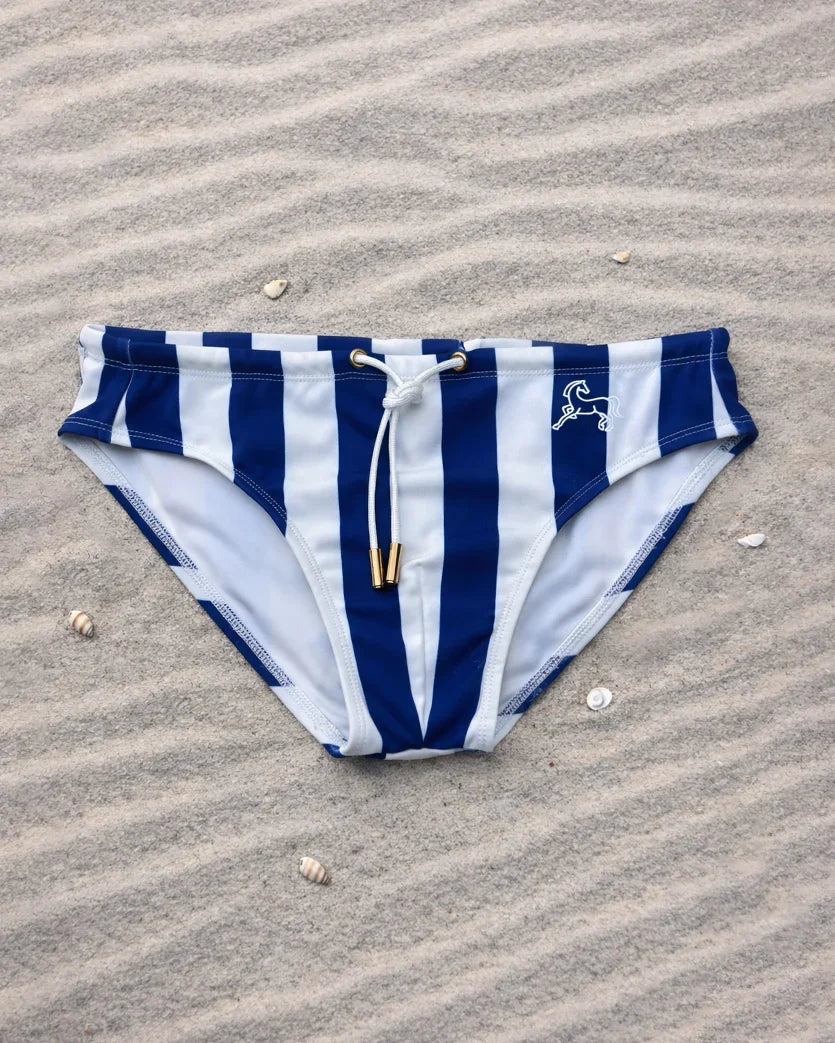 Palm Stallion blue and white striped swim briefs on sand with shells