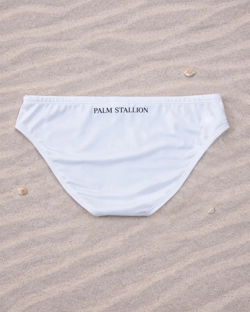 Palm Stallion white briefs back view on sand with shells, minimalist beachwear